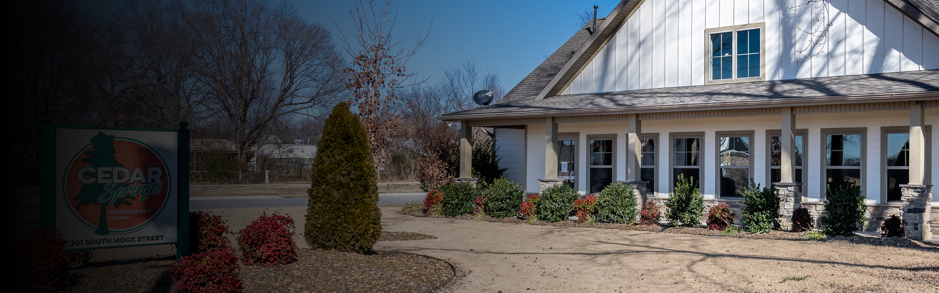 Front view of Cedar Springs Independent Living building with white siding, stone columns, and a landscaped front yard.