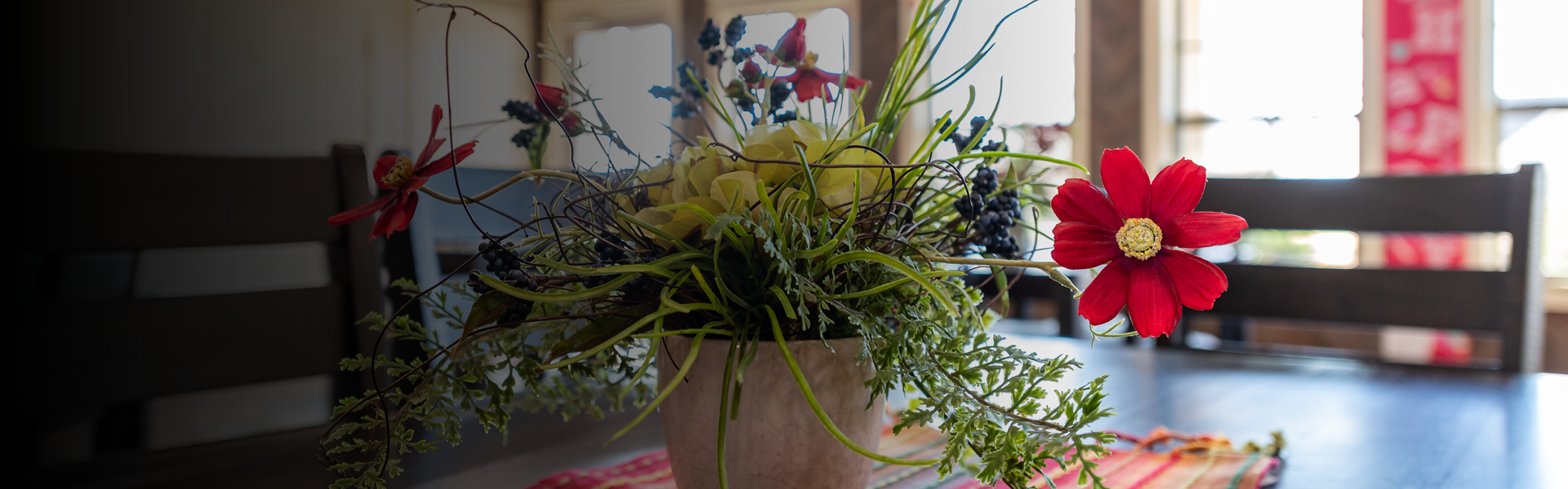 Vase with a colorful floral arrangement on a dining table, with vivid red blossoms as the focal point on the right.