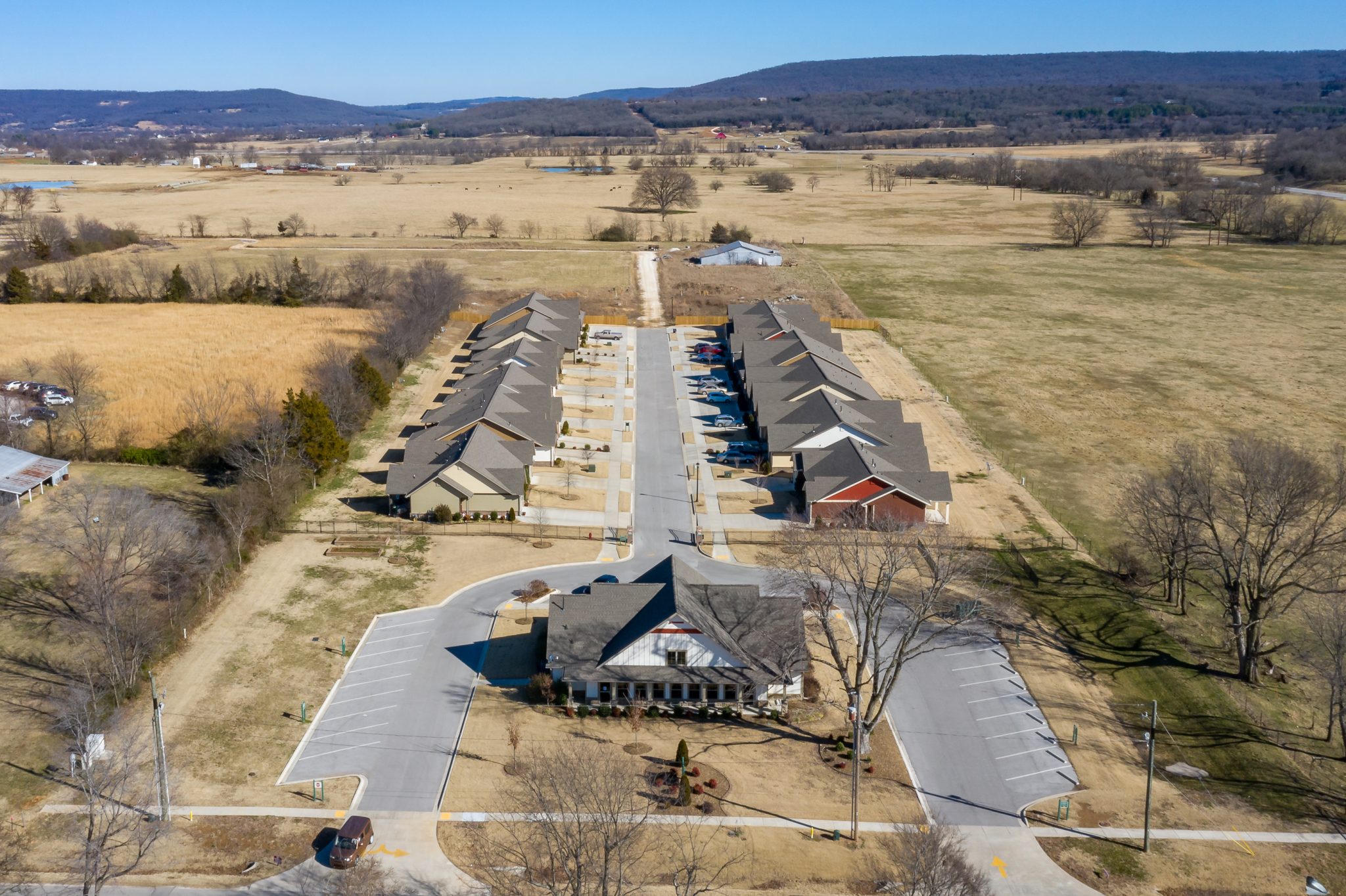 Aerial view of a residential townhouse complex with rows of homes along a central road, set in a rural, open landscape.