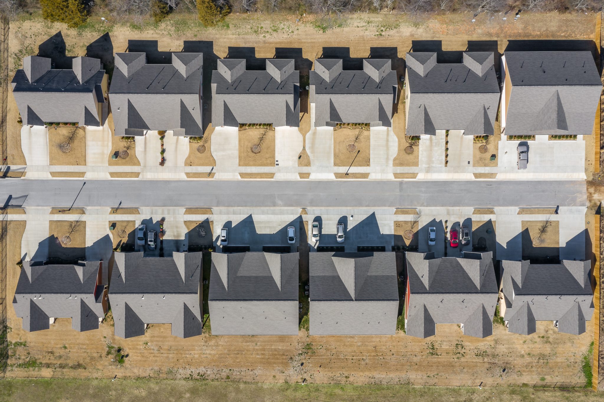 Top-down view of a row of gray-roofed townhouses with driveways and parked cars along a street