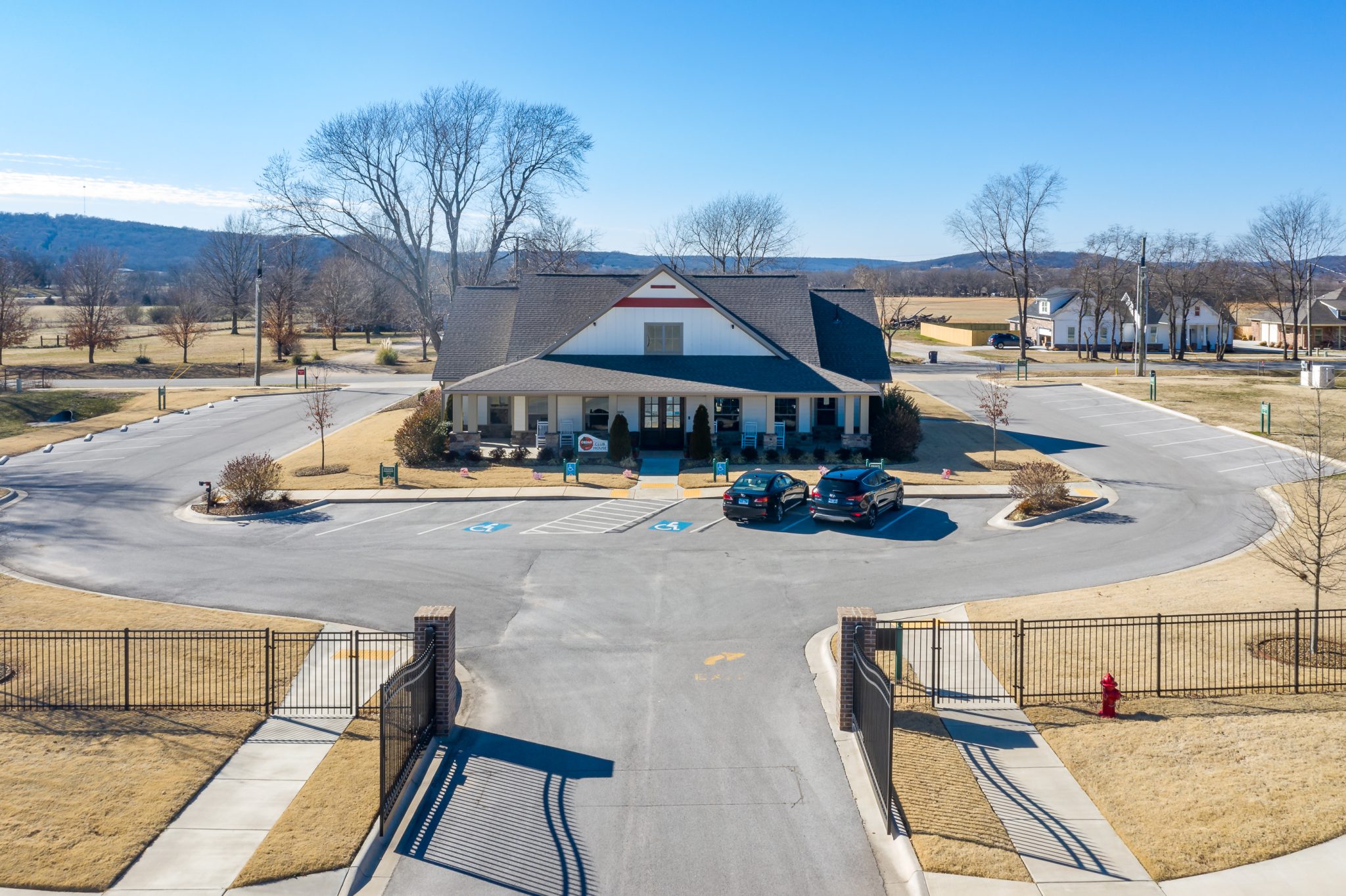 Clubhouse-style building with a peaked roof in a large parking lot under a clear blue sky, surrounded by bare trees in winter.